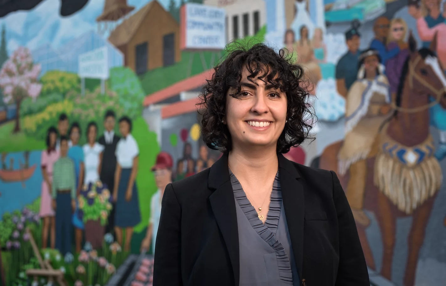 Photo of Darya Farivar, standing in front of a street mural featuring families of different communities.